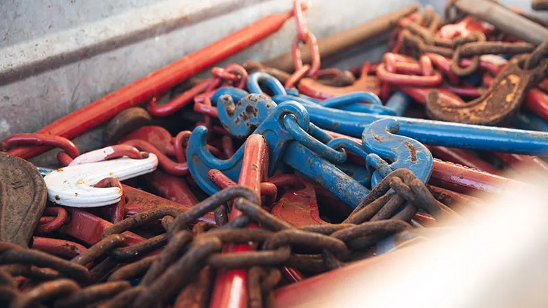 Eine Nahaufnahme eines Stapels von Metallketten und bunten Haken, darunter blaue, rote und weiße Teile, die in einem Metallbehälter verheddert sind.