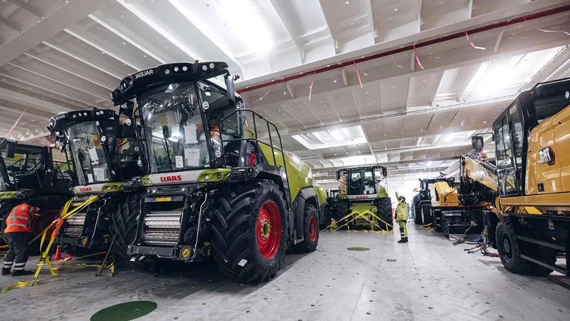 Stevedoring and port logistics In a brightly lit, spacious industrial facility, several large agricultural and harvesting machines are parked and inspected by workers in protective clothing. Yellow tape cordons off the areas around the machines.